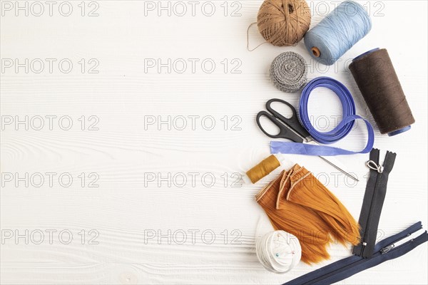 Sewing accessories: scissors, thread, thimbles, braid on white wooden background. Top view, flat lay, copy space