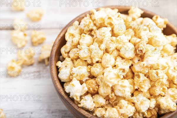 Popcorn with caramel in wooden bowl and a cup of coffee on a white wooden background and linen textile. Side view, close up, selective focus