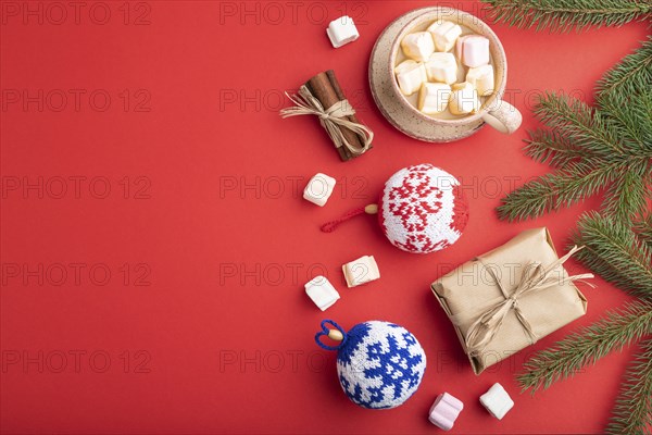 Christmas or New Year composition. Decorations, box, cinnamon, knitted balls, fir and spruce branches, cup of coffee, on a red paper background. Top view, copy space, flat lay