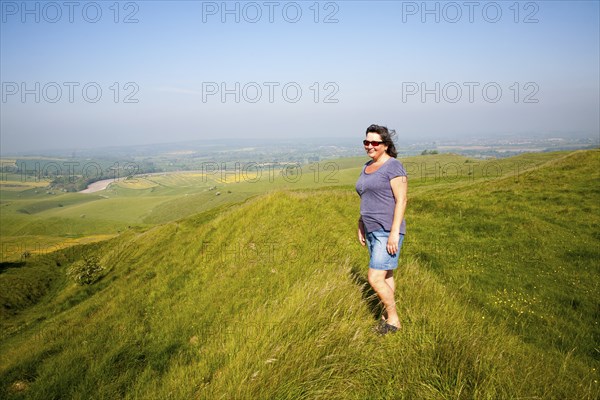 Woman standing on steep chalk scarp slope on downland at Cherhill Down, Wiltshire, England, United Kingdom, Europe