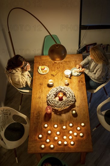 Symbolic image energy saving, cold winter, energy crisis, cold flat, mother and daughter dressed warmly at dinner, only one lamp on, candlelight, heating on to a minimum