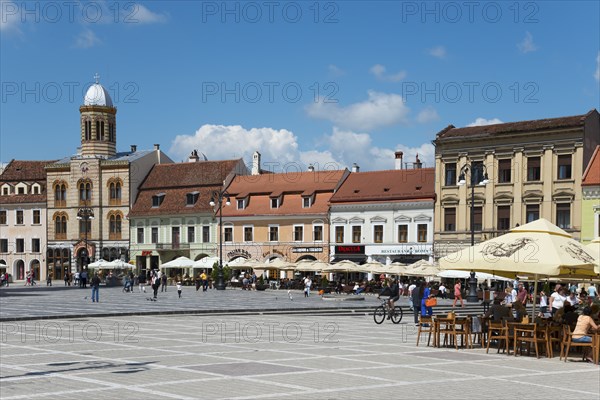 Lively market square with people and cafés, historic facades and parasols in sunny weather, Church of the Assumption of the Virgin Mary and town houses on the market square Piata Sfatului, Old Town, Brasov, Transylvania, Romania, Europe