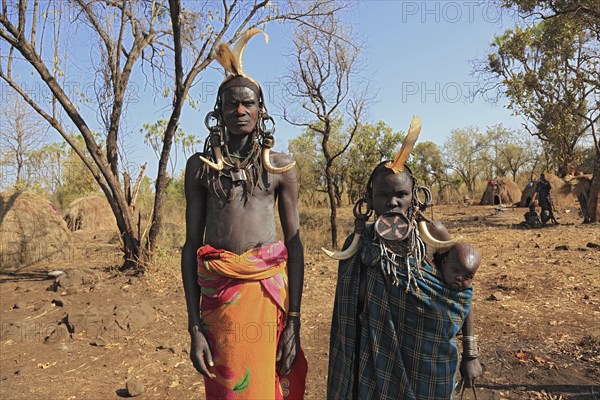 Southern Ethiopia, in Maco National Park, Mursi tribe, Mursi man, Mursi woman with baby, painted skin and headdress, plate-lipped woman, woman with plate in lower lip, Ethiopia, Africa