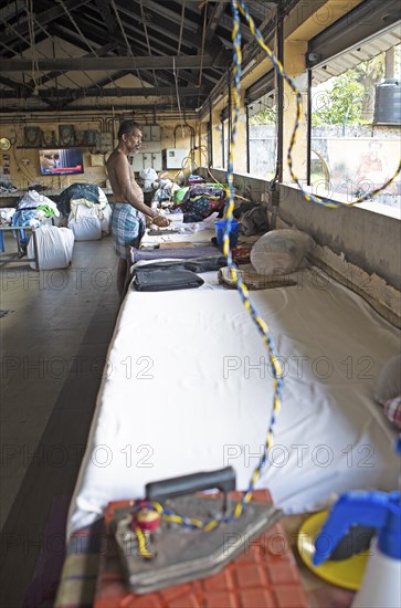 Indian man ironing laundry at Dhoby Khana laundry, Kochi, Kerala, India, Asia