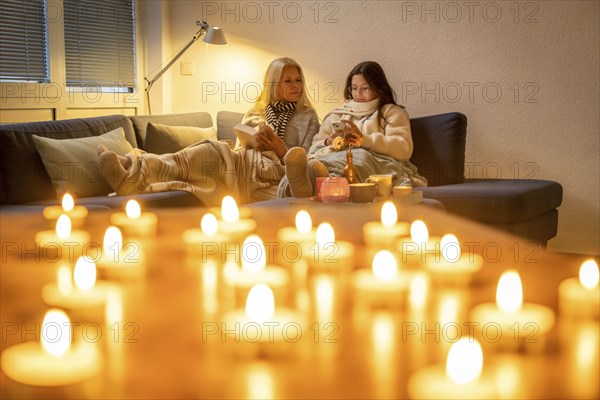 Symbolic image energy saving, cold winter, energy crisis, cold flat, mother and daughter lying on the sofa, warmly dressed, candlelight, heating on to a minimum