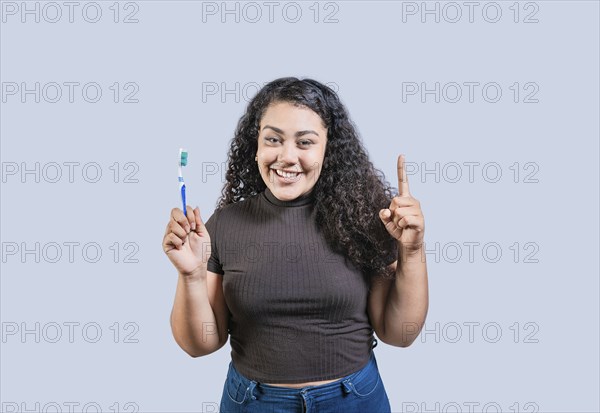 Happy young woman holding toothbrush pointing up. Smiling girl holding toothbrush and pointing up