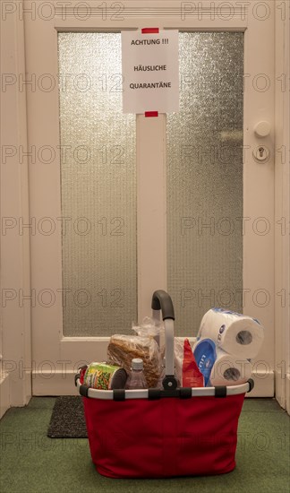 Symbolic image Domestic quarantine, man is in isolation at home due to a suspected corona infection, warning sign for visitors on the front door, communicates with a visitor through the door, neighbours have been shopping and put the things in front of the door