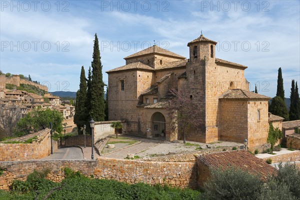 A medieval stone church surrounded by cypress trees in a tranquil Mediterranean landscape under a blue sky, Parish Church of San Miguel, Alquézar, Alquezar, Huesca, Aragón, Aragon, Pyrenees, Spain, Europe