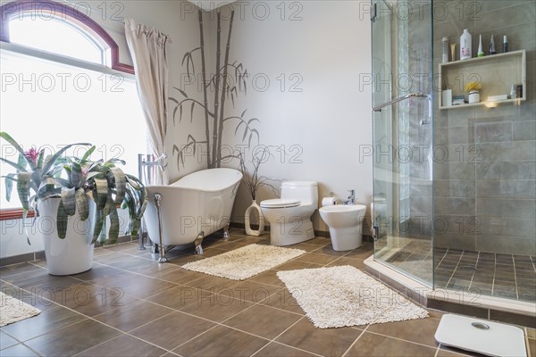 Freestanding bathtub, bidet, clear glass shower stall in en suite with grey nuanced ceramic tile floor on upstairs floor inside a luxurious residential home, Quebec, Canada, North America