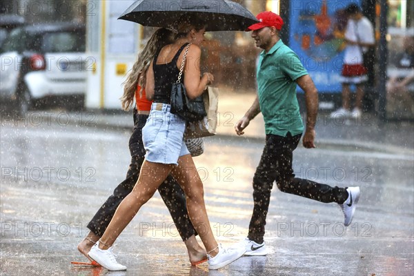 Two woman and a man run across Potsdamer Strasse in heavy rain. After weeks of heat, the first heavy rain brought cooling, Berlin, 15.08.2022