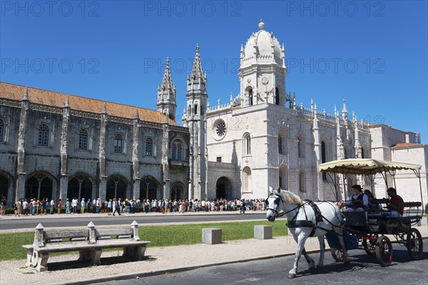 Eine gotische Kathedrale unter klarem blauen Himmel mit Touristen und einer Kutsche mit Pferden im Vordergrund, Hieronymus Kloster, Mosteiro dos Jerónimos, Hieronymitenkloster, Weltkulturerbe, Klosterkirche Santa Maria, Belém, Belem, Bethlehem, Lissabon, Lisboa, Portugal, Europe