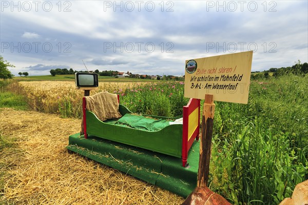 Colourful outdoor wooden bed on straw, vintage TV with antenna, original hiking trail in the poppy field, sign with inscription, Please do not disturb, We sleep in the poppy field, Germerode, Meißner, Geo-nature park Park Frau-Holle-Land, Hesse, Germany, Europe