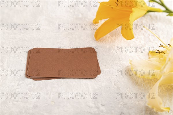 Brown paper business card mockup with orange day-lily flower on gray concrete background. Blank, side view, copy space, still life. spring concept