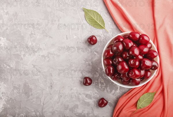 Fresh red sweet cherry in white bowl on gray background with red textile. top view, flat lay, copy space