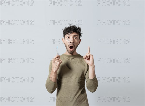 Amazed young man holding toothbrush pointing up. Guy with surprised gesture holding toothbrush pointing an advertisement