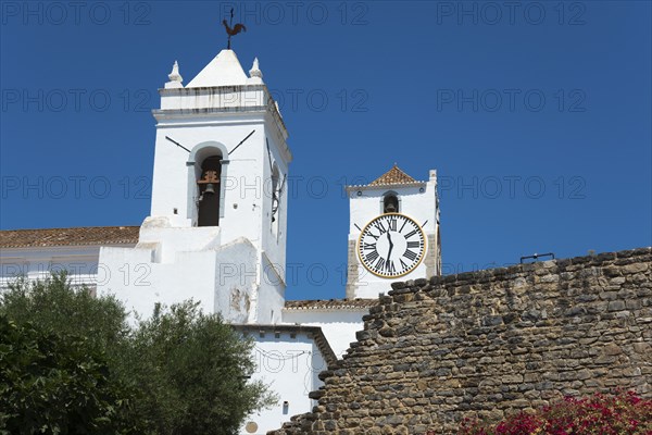 Two church towers with clocks, a wall in the foreground against a bright blue sky, Santa Maria do Castelo church, Tavira, Faro, Algarve, Portugal, Europe