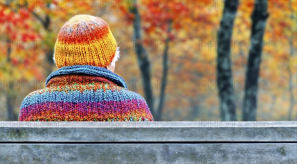 A senior citizen enjoys the view of autumnal nature in colourful knitwear, generated with AI, AI generated