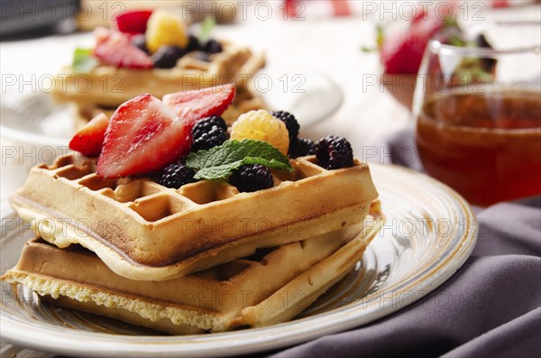 CLoseup view at belgian waffles served with strawberries and blackberries on kitchen table