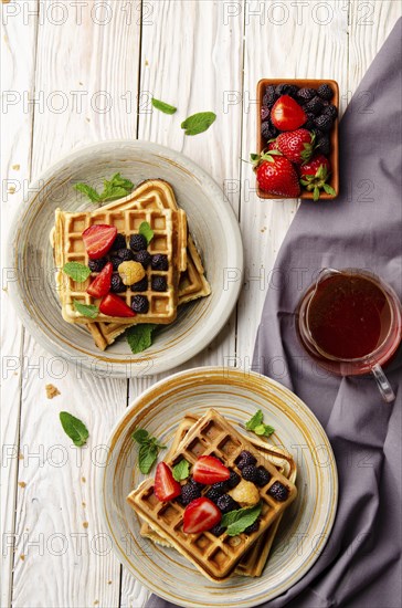 Flat view at belgian waffles served with strawberries and blackberries on white wooden kitchen table closeup