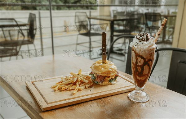 Big hamburger with fries and milkshake on restaurant table. Classic burger with fries and milkshake on wooden board with copy space