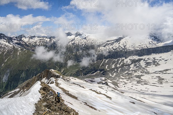 Mountaineer on a rocky ridge with snow, descent from the summit of Schönbichler Horn, view of snow-covered mountain peaks and valley Zemmgrund, Berliner Höhenweg, Zillertal Alps, Tyrol, Austria, Europe