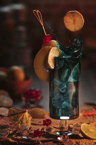 Sparkling cocktail in a glass with ice cube cubes, decorated with lime slices and cherries on a sandy background in a sunset atmosphere