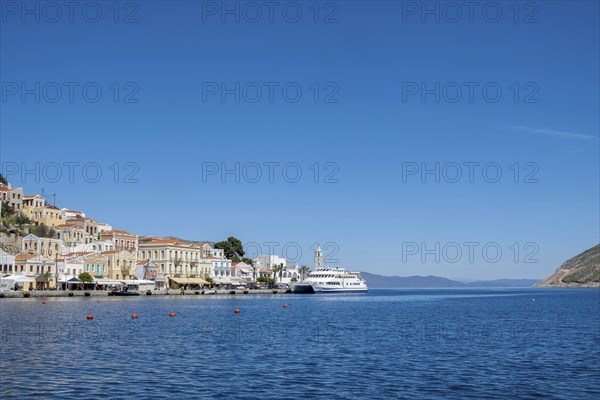 A picturesque coastal town with white houses and a boat in the clear blue sea under a bright blue sky, Symi Island, Dodecanese, Greek Islands, Greece, Europe