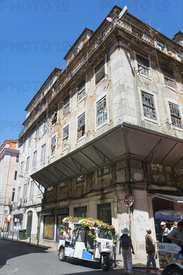 Dilapidated historic building with a tuk-tuk on a street under a clear blue sky, Rua Nova do Carvalho, Lisbon, Lisboa, Portugal, Europe