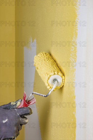 Wall is painted with yellow paint, hand with paint roller