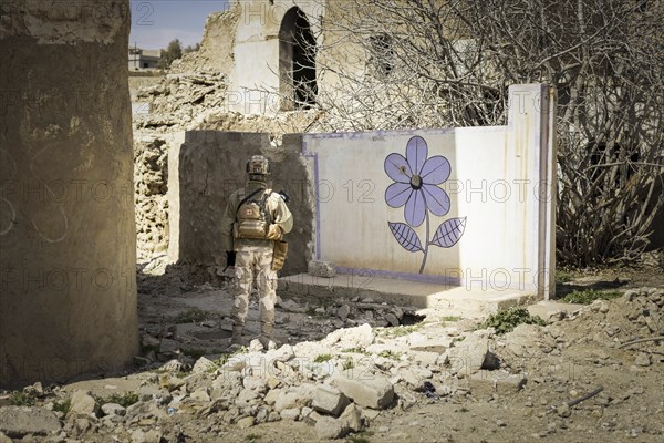 Ein Soldat steht vor einer an die Wand gemalten Blume im zerstoerten Stadtzentrum von Sinjar, 09.03.2023