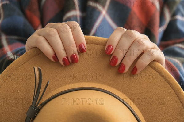 Stylish red female nails. Woman in poncho holding brown trendy hat. Modern Beautiful manicure. Autumn winter nail design concept of beauty treatment. Gel nails. Skin care. Wellness. Trendy colors