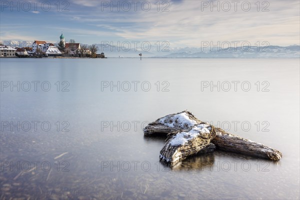 Wooden trunk and picturesque church of St George on the lakeshore in front of snow-covered Pfänder on a clear winter's day, moated castle, Lake Constance, Bavaria, Germany, Europe