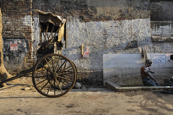 24.02.2011, Kolkata, West Bengal, India, Asia, A rickshaw driver washes himself next to his wooden rickshaw on a roadside in Kolkata, the only city in India where hand-pulled rickshaws still exist, Asia