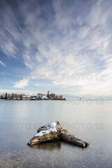 A peaceful lake with a log in the foreground with picturesque St George's Church on the lakeshore in front of snow-covered Pfänder on a clear winter's day, moated castle, Lake Constance, Bavaria, Germany, Europe