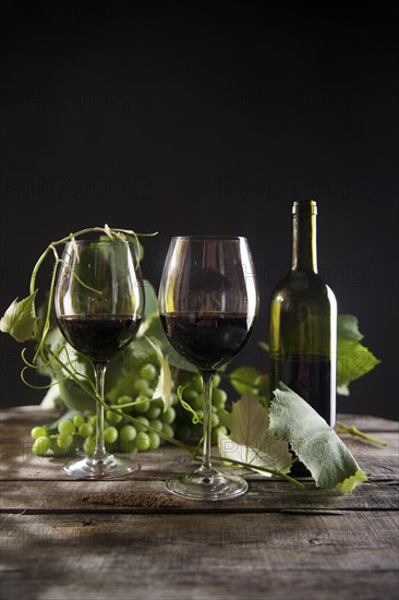 Glass of red wine with bottle and bunch of sour grapes on a black background