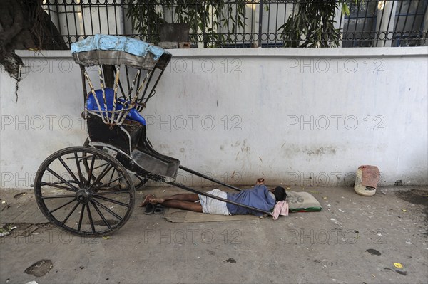 25.02.2011, Kolkata, West Bengal, India, Asia, A rickshaw driver sleeps next to his wooden rickshaw on a roadside in Kolkata, the only city in India where hand-pulled rickshaws still exist, Asia