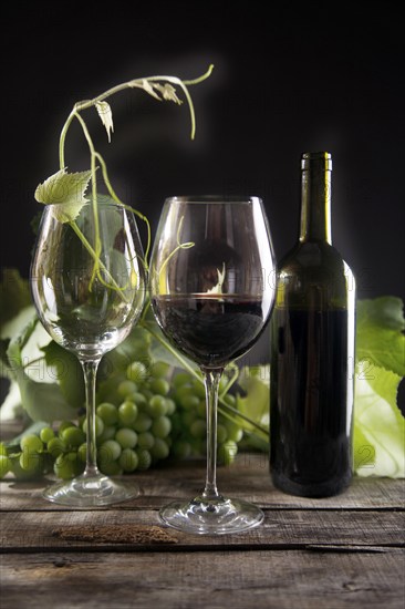 Glass of red wine with bottle and bunch of sour grapes on a black background