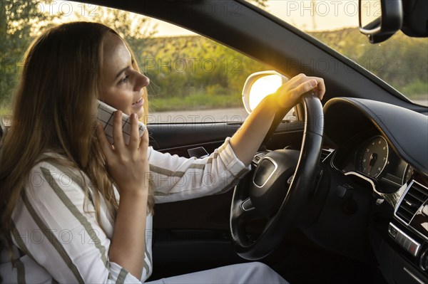 Happy young woman speaking by mobile phone while driving car. Business woman talking phone call in automobile. Unsafely risky driving. Concept of multitasking