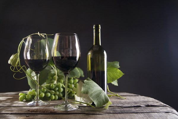 Glass of red wine with bottle and bunch of sour grapes on a black background