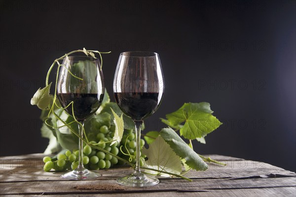 Glass of red wine with bottle and bunch of sour grapes on a black background