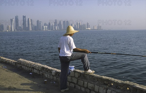 13.09.2010, Doha, Qatar Qatar, A man fishing on the promenade along Al Corniche Street with a view of the skyline of the Al Dafna business district in the background