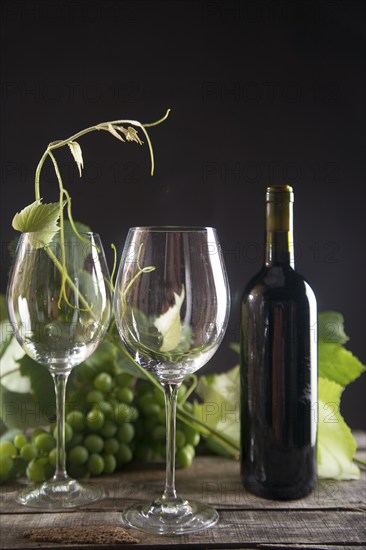 Glass of red wine with bottle and bunch of sour grapes on a black background