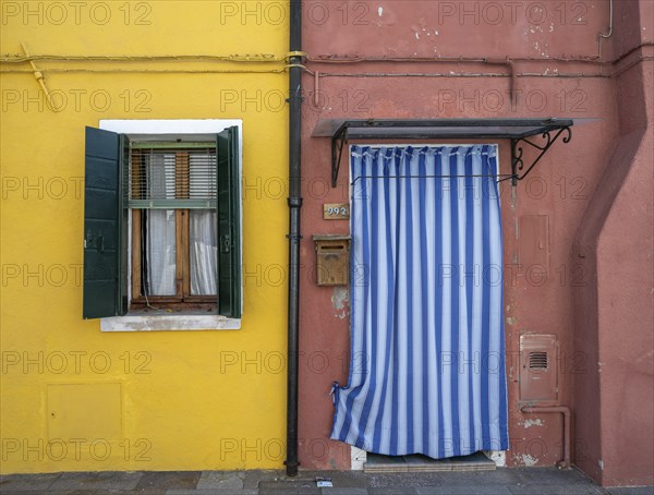 Red and yellow house facade with entrance door with blue and white curtain and windows, colourful houses on the island of Burano, Venice, Veneto, Italy, Europe