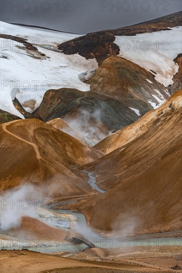 Bridge over steaming stream between colourful rhyolite mountains with snowfields, Hveradalir geothermal area, Kerlingarfjöll, Icelandic highlands, Iceland, Europe