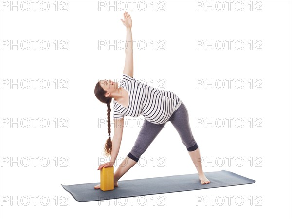 Pregnancy yoga exercise, pregnant woman doing asana Utthita trikonasana, extended triangle pose with block isolated on white background