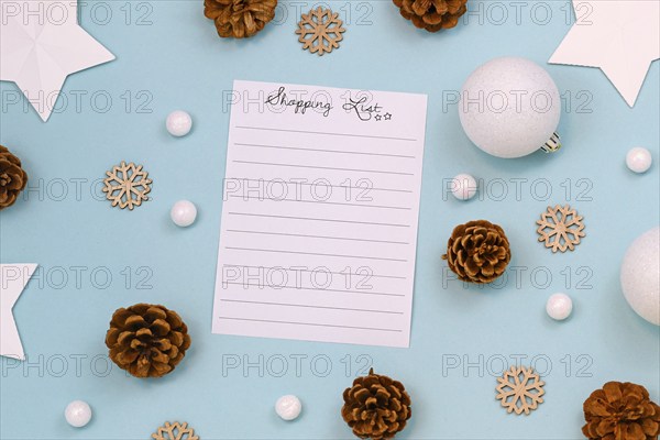 Concept for Christmas shopping with top view flat lay with empty shopping check list and seasonal decorations like tree baubles, snowflakes, stars and for cones on blue background