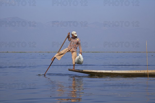 Intha fisherman steering traditional fishing boat by wrapping his leg around the oar, Inle Lake, Nyaungshwe, Shan State, Myanmar, Burma, Asia