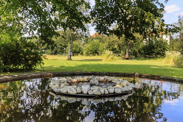 Small fountain and water bowl with stones under trees, Schlehdorf Monastery, Bavaria, Germany, Europe