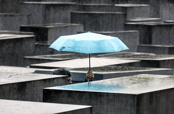 A visitor to the Memorial to the Murdered Jews of Europe protects himself from heavy rain with an umbrella, Berlin, 23 June 2023