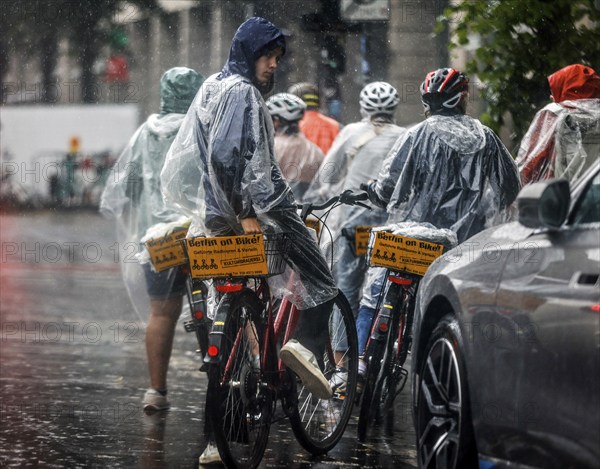 Tourists on a Berlin On Bike cycling tour protect themselves from heavy rainfall with rain capes, Berlin, 23 06 2023